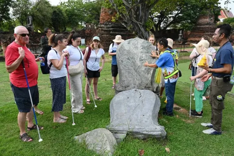 A group of visually impaired tourists exploring a stone sculpture at a heritage site with a guide