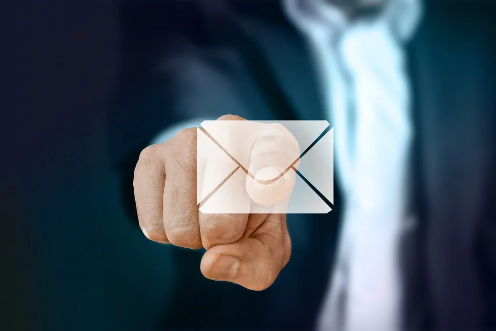 A person in a suit pointing at the camera with a translucent envelope icon overlay, symbolizing email contact