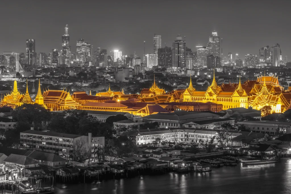 Illuminated Grand Palace in golden tones with modern Bangkok skyline in black and white background