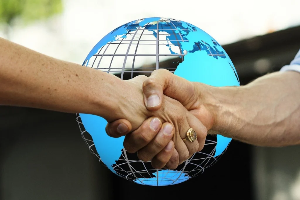 Two hands shaking with a digital globe overlay, symbolizing global cooperation and inclusive tourism
