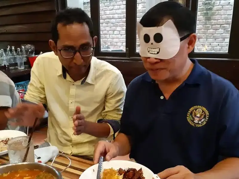 Two guide trainees sharing a meal, one wearing a blindfold to simulate visual impairment