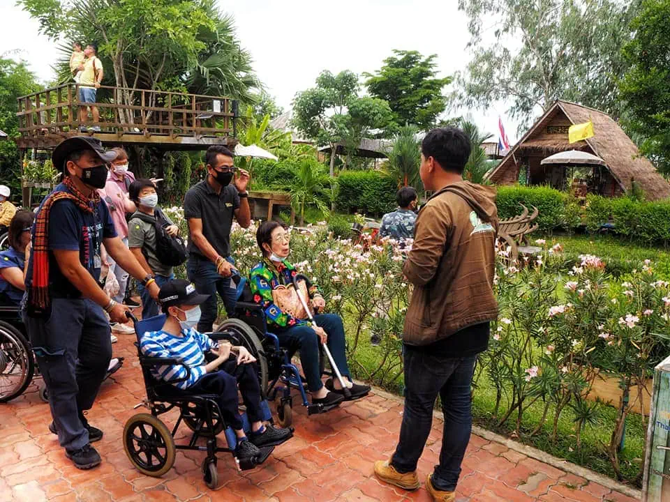 A diverse group of tourists, including wheelchair users, exploring a garden path in a cultural village