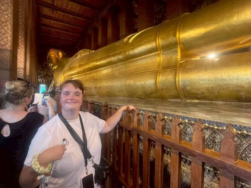 A smiling tourist posing in front of the Reclining Buddha statue at Wat Pho, Bangkok
