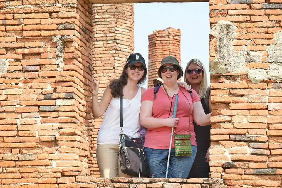 Three smiling tourists, including one with a white cane, standing in a brick window at a heritage site
