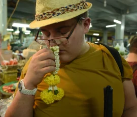 Bangkok through the senses—where fragrance, texture, and culture guide the way A visually impaired traveler smelling a flower garland in a vibrant Bangkok market while holding a cane.