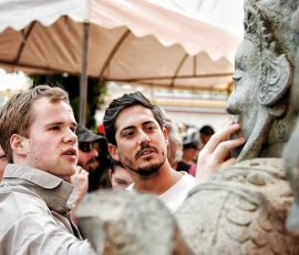 Discover Wat Po through touch—where ancient wisdom meets inclusive exploration A blind traveler touching the face of a stone statue at Wat Po, surrounded by companions in an outdoor cultural setting