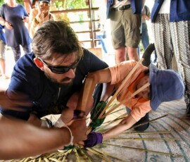 A tactile cultural experience: learning the delicate art of bamboo weaving at Ban Dok Bua. A blind male traveler wearing sunglasses guided by a local Thai woman while learning traditional bamboo basket weaving in Ban Dok Bua village.