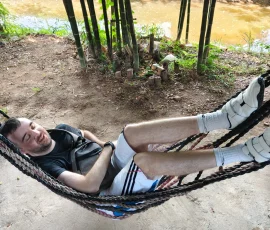 Finding a moment of perfect peace and tranquility by the riverside. A traveler resting comfortably in a rope hammock under the shade of trees near a river at Baan Dok Bua village.