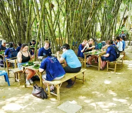 A refreshing organic lunch served in the peaceful heart of the village's bamboo garden. A group of international travelers enjoying a traditional Thai lunch on bamboo tables in a shaded bamboo garden.