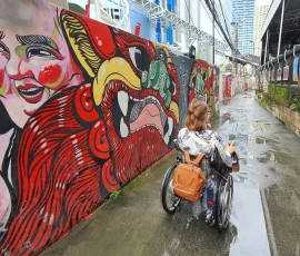 Discover Bangkok’s creative pulse through accessible urban pathways and cultural expression A wheelchair user navigating a narrow alleyway with vibrant street art and photo displays in Bangkok