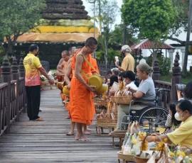 Inclusive cultural experiences in Northern Thailand—where tradition welcomes everyone A wheelchair user participating in a morning almsgiving ceremony with Buddhist monks on a wooden bridge in Northern Thailand
